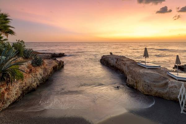 Sonnenuntergang am Strand des Star Beach Village und Water Park mit ruhigen Wellen und Felsen.