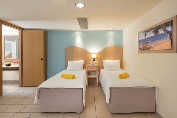 Zwei Betten im Star Beach Village Zimmer mit gelben Handtüchern und einem Nachttisch dazwischen.