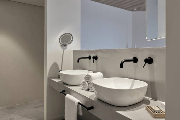 Badezimmer im Caravel Hotel mit zwei weißen Waschbecken und schwarzen Armaturen.