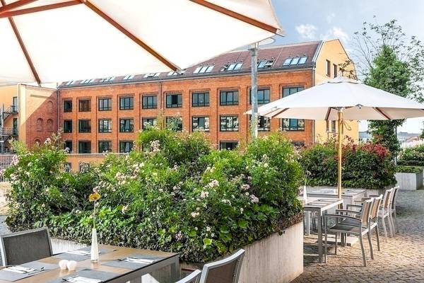 Außenbereich des NH Berlin Alexanderplatz Hotels mit Tischen und Stühlen unter Schirmen.
