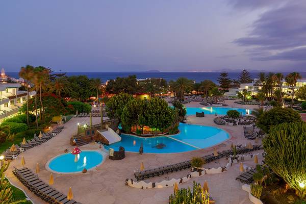 Abendausblick auf den Swimmingpool des H10 Lanzarote Princess Hotels mit Sonnenliegen und tropischen Pflanzen.