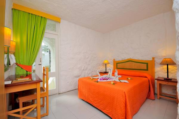 Zimmer im Casuarina Resort & Spa mit Bett, Tisch und zwei Lampen auf Nachttischen.