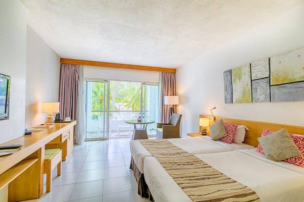 Innenansicht eines Doppelzimmers im Casuarina Resort & Spa mit zwei Betten, Schreibtisch und Balkon.