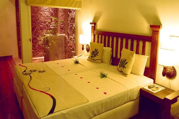 Doppelbett-Zimmer im Siddhalepa Ayurveda Gesundheitsresort mit zwei Betten, cremefarbenen Laken und Kissen, und einer Aussicht auf eine Steinmauer mit Pflanzen.