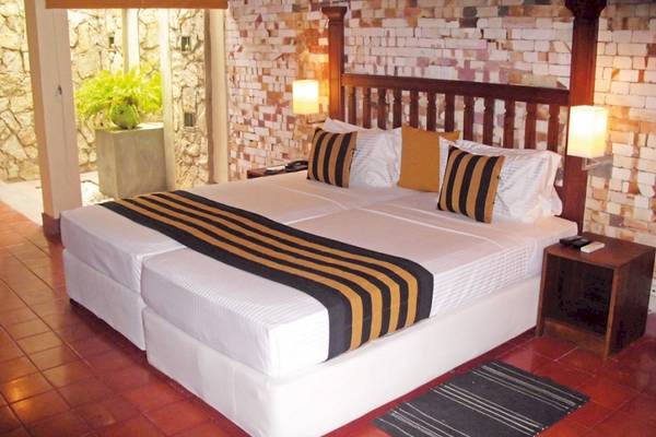 Doppelbett im Zimmer des Siddhalepa Ayurveda Gesundheitsresorts mit bunten Kissen und einer Ziegelwand.