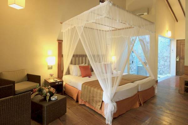 Doppelbett im Siddhalepa Ayurveda Gesundheitsresort mit Bettwäsche, Kissen und Vorhängen.