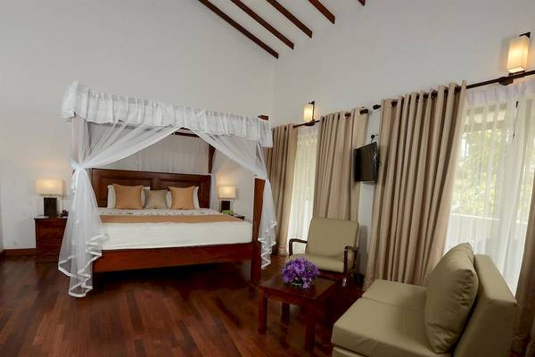 Schlafzimmer im Siddhalepa Ayurveda Health Resort mit vierposterbett, bettwäsche, kissen, nachttischen, lampen und fernseher