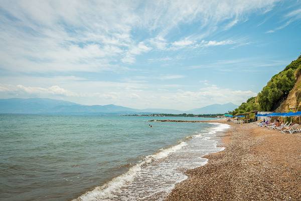 Strand des Pavlina Beach Hotels mit weißen Sonnenliegen und blauen Sonnenschirmen.
