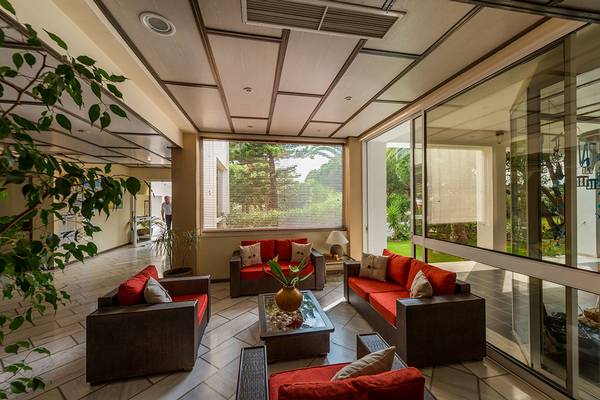 Lobby-Lounge im Pavlina Beach Hotel mit roten Sofas, Glaswänden und Pflanzen.