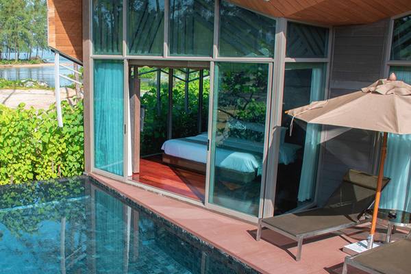 Außenansicht des Kalima Resort & Villas Khao Lak mit Zimmer, Pool, Sonnenschirm und Lounge-Stühlen.
