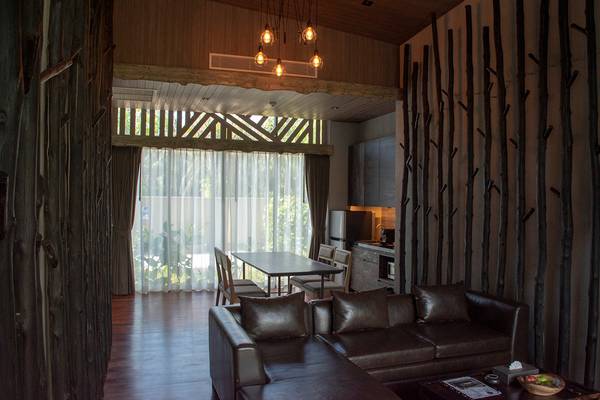 Wohnzimmer im Kalima Resort & Villas Khao Lak mit Ledersofa, Tisch und Fenstern.