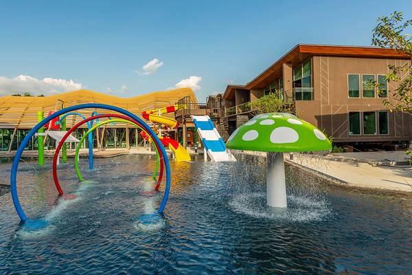 Außenpool des Kalima Resort & Villas Khao Lak mit bunten Wasserspielen und einem grünen Pilzbrunnen.