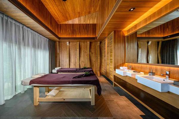 Massageraum im Kalima Resort & Villas Khao Lak mit zwei Massagetischen, holzvertäfelten Wänden und Waschbecken.