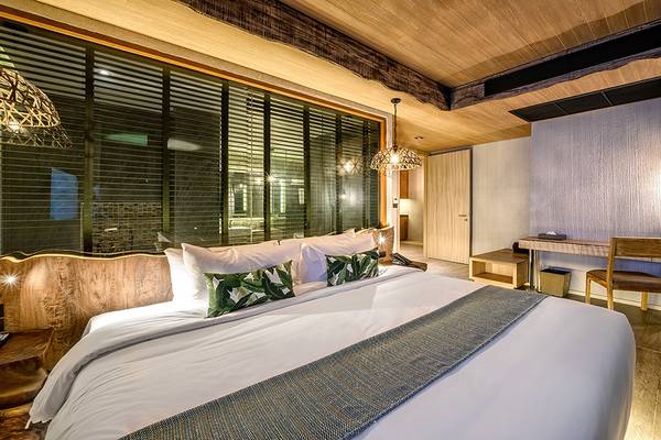 Innenansicht eines Hotelzimmers im Kalima Resort & Villas Khao Lak mit einem großen Bett, Fenstern und Holzmöbeln.