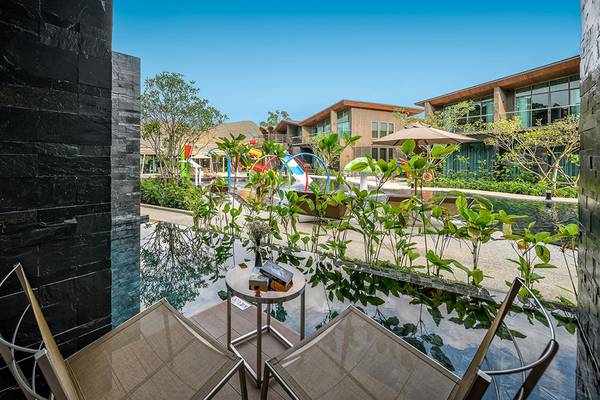 Blick vom Balkon des Kalima Resort & Villas Khao Lak auf eine grüne Anlage mit einem kleinen Tisch