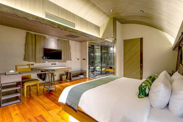 Innenansicht des Schlafzimmers im Kalima Resort & Villas Khao Lak mit Holzboden, Fernseher, Schreibtisch und Badezimmer