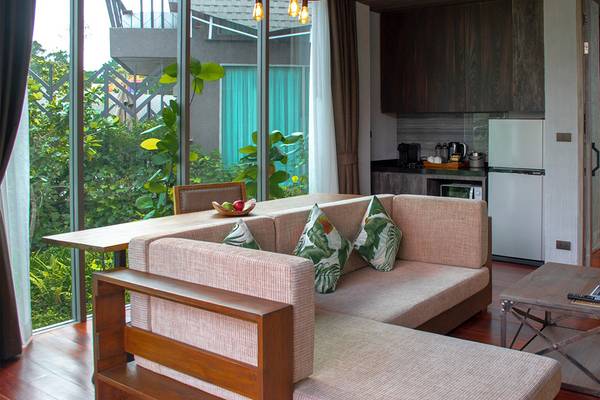 Wohnbereich im Kalima Resort & Villas Khao Lak mit großem Fenster, Couch, Esstisch und Kühlschrank.