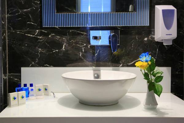 Ein Badezimmer im LABRANDA Ephesus Princess Hotel mit schwarzen Marmorfliesen, einem weißen Waschbecken und blauen Blumen in einer Vase.