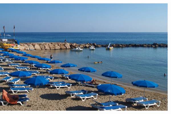 Strand des Cavo Maris Beach Hotels mit vielen Liegen und blauen Sonnenschirmen