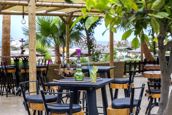 Terrasse des Cavo Maris Beach Hotels mit Tischen, Stühlen und einem grünen Wasserpfeifenset.