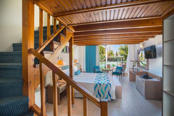 Innenansicht eines Zimmers im Cavo Maris Beach Hotel mit Bett, Stairs, Möbeln und Fernseher.