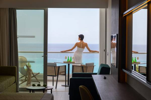 Frau in weissem Kleid auf dem Balkon der Cavo Maris Beach Suite mit Meerblick