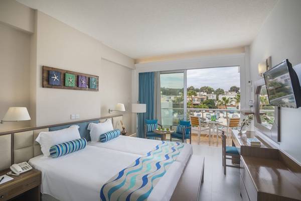 Ein modernes Hotelzimmer mit zwei Betten, Blick auf die Terrasse und einen Swimmingpool.