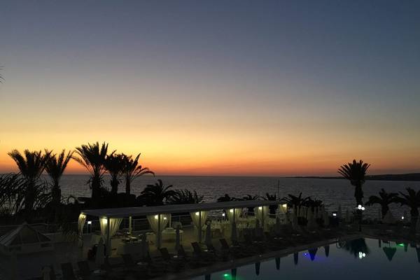 Abendlicher Blick auf den Pool im Queens Bay Hotel mit Sonnenuntergang am Horizont.