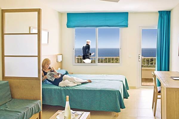 Eine Frau liegt auf einem Bett im Hotelzimmer mit Blick auf das Meer.