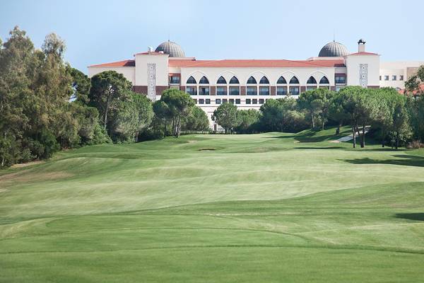 Golfplatz vor dem Kempinski Hotel The Dome Belek mit Bäumen und Gebäude im Hintergrund.