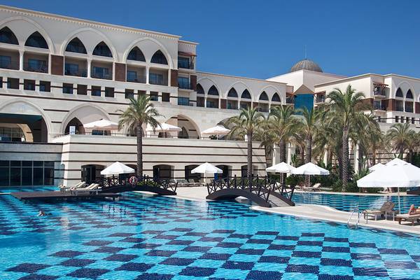 Außenbereich des Kempinski Hotel The Dome Belek mit Pool, Liegestühlen und Palmen