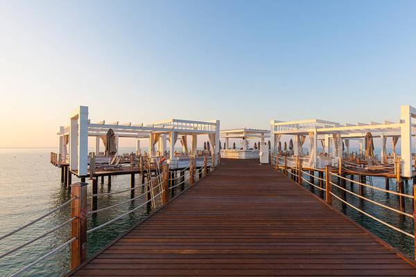 Außenterrasse des Kempinski Hotel The Dome Belek mit weißen Pavillons und Holzbrücke über dem Wasser
