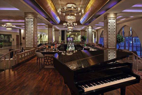 Lobby-Bereich des Kempinski Hotel The Dome Belek mit Klavier, Bar und eleganter Einrichtung.