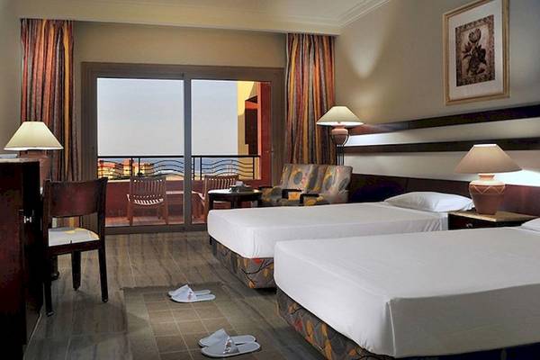 Doppelzimmer im Malikia Resort Abu Dabbab mit zwei Betten, Fernseher, Schreibtisch und Balkon mit Meerblick.