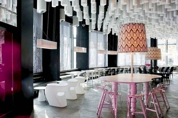 Innenbereich des Barcelo Raval Hotels mit pinken und weißen Möbeln, großen Fenstern und einer weißen Decke mit Lampen.