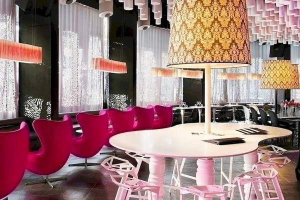 Inneneinrichtung des Barcelo Raval Restaurants mit pinken Stühlen, weißen Tischen und goldenen Lampen.