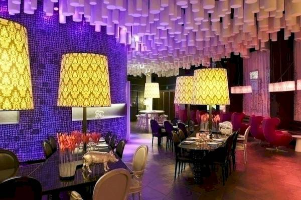 Das elegante Interieur des Barcelo Raval Hotels mit violetten Wänden, goldenen Lampenschirmen und modernen Möbeln.