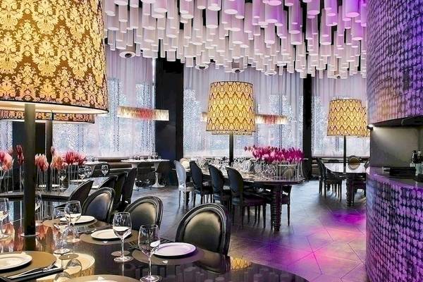 Innenansicht des Barcelo Raval Restaurants mit violetten Wänden, goldenen Kronleuchtern und gedeckten Tischen.