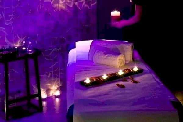 Spa-Behandlungsraum im Barcelo Raval Hotel mit violettem Licht und Kerzen auf einem Tisch.