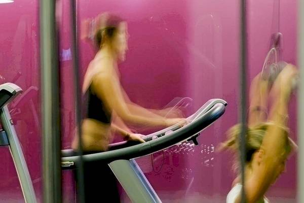 Frau auf dem Laufband im Fitnessstudio mit pinker Wand im Hintergrund