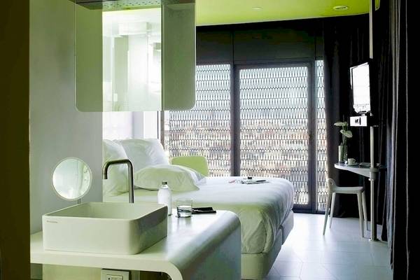 Innenansicht eines Zimmers im Barcelo Raval Hotel mit Bett, Schreibtisch, Fernseher und Badezimmer.