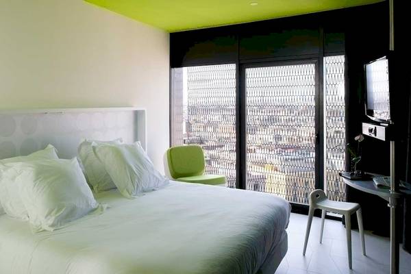 Innenansicht eines Hotelzimmers im Barcelo Raval Hotel mit Bett, grünem Stuhl und Fernseher.