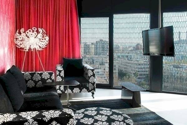 Wohnzimmer im Barcelo Raval Hotel mit schwarzem und weißem Sofa, roter Vorhang, Tisch, Fernseher und Lampen.