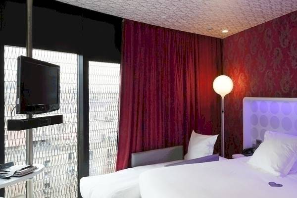 Hotelzimmer im Barcelo Raval mit Fernseher, Lampen und roten Vorhängen.