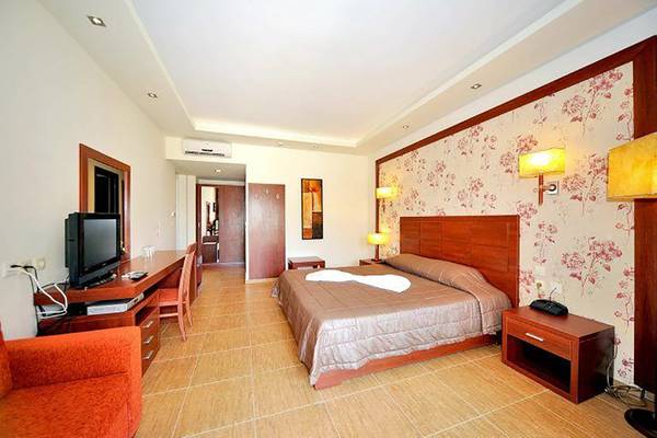 Schlafzimmer im Gaia Palace Hotel mit einem Bett, Fernseher, Schreibtisch und einem orangefarbenen Stuhl.