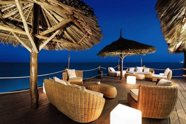 Abendliche Terrasse im Melia Zanzibar mit Blick auf das Meer, umgeben von Korbmöbeln und Strohdächern.