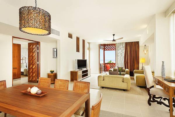 Innenansicht des Wohnzimmers im Melia Zanzibar Hotel mit Esstisch, Sofas und Fernseher.