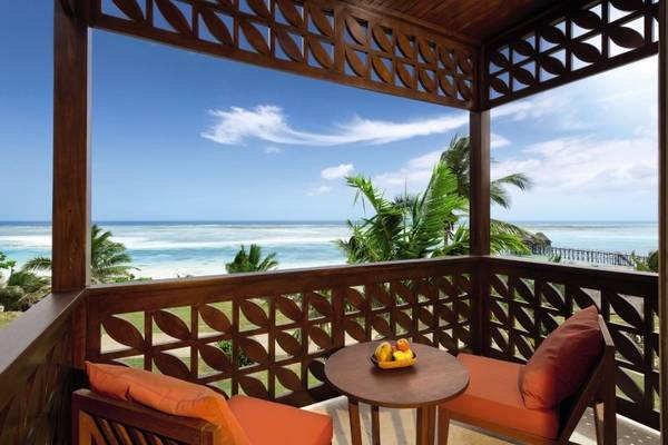 Balkon des Melia Zanzibar Hotels mit Blick auf das Meer und zwei roten Stühlen mit Kissen.