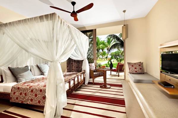 Schlafzimmer im Melia Zanzibar Hotel mit Himmelbett, Fernseher und Aussicht auf Palmen.