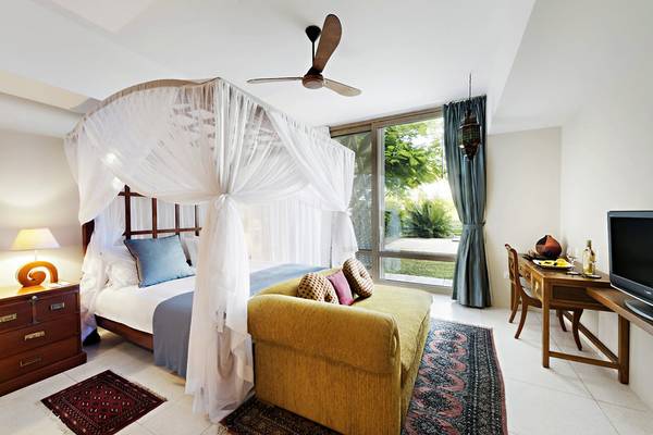 Schlafzimmer im Melia Zanzibar Hotel mit Bett, gelbem Sofa, Tisch und Fernseher.